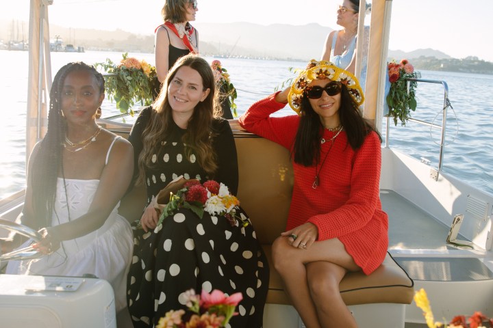 Three women sitting on a boat adorned with flowers on a sunny day.