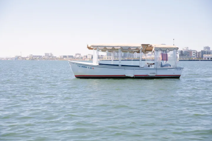 A small boat with a canopy floats on water, city skyline in the background.