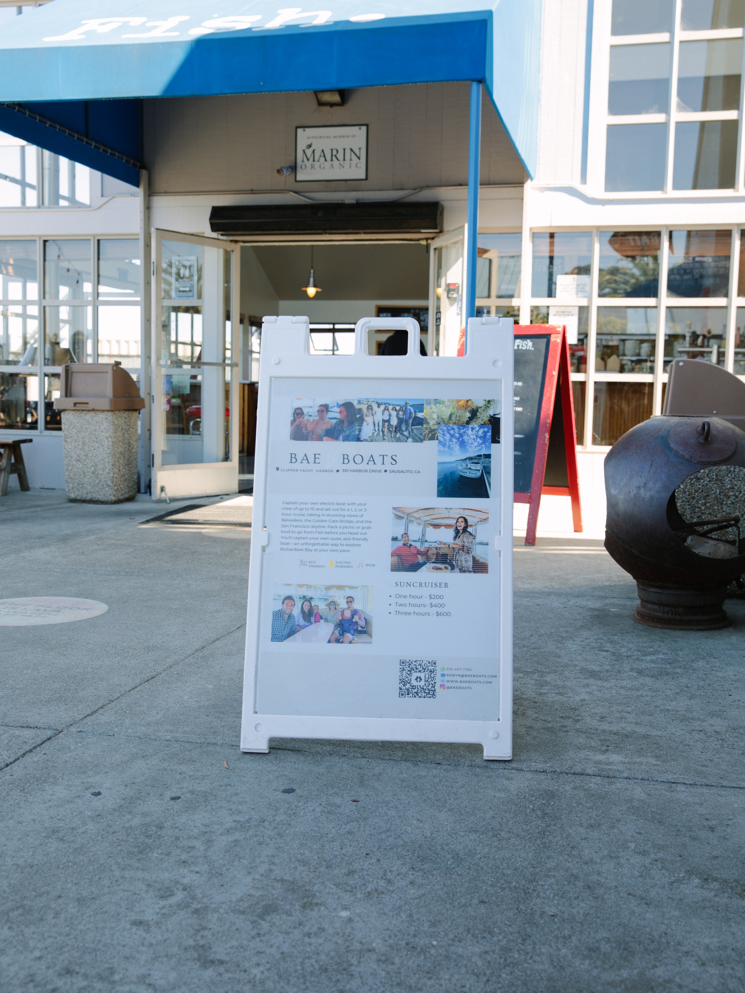 A-frame sign for Bae Boats outside a building with a blue awning labeled 'fish.'