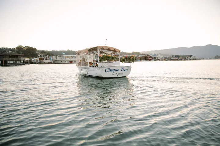 A boat named Cinque Terre on a calm body of water with houses in the background.