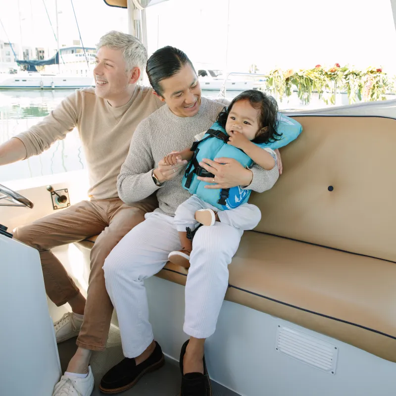 Two adults smiling with a child in a life jacket on a boat.