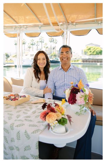 Smiling couple seated on a boat with floral centerpiece on table.