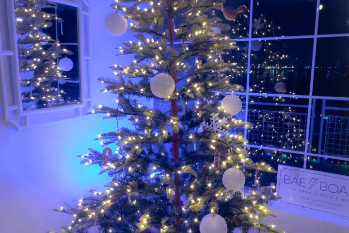 Christmas tree with lights and large ornaments by a window, reflected in a mirror.